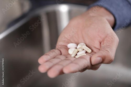 Hand open showing various pills, hand holding pills over kitchen sink