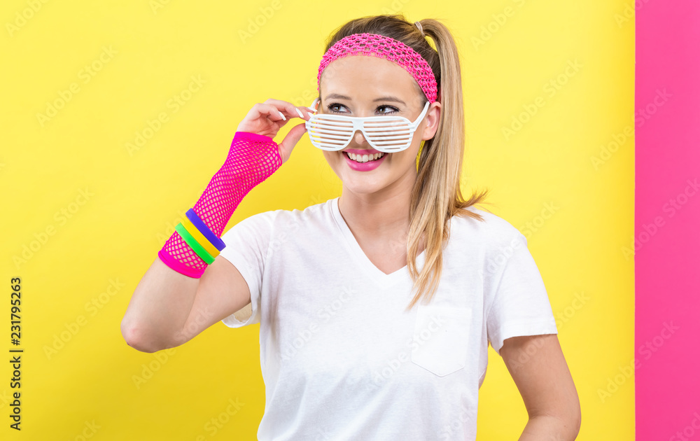 Woman in 1980's fashion with shatter shade glasses on a split yellow and pink background Woman in 1980's fashion with shatter shade glasses on a split yellow and pink background
