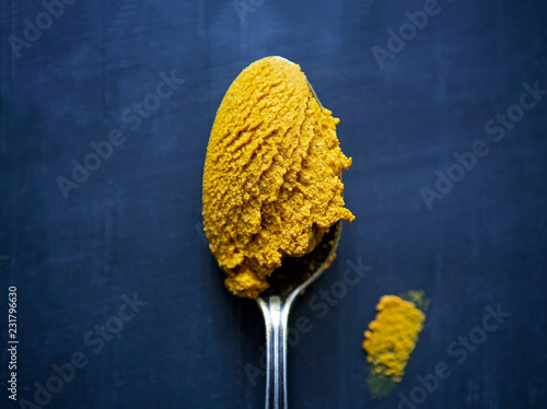 Turmeric paste in a spoon rests on a blue surface.