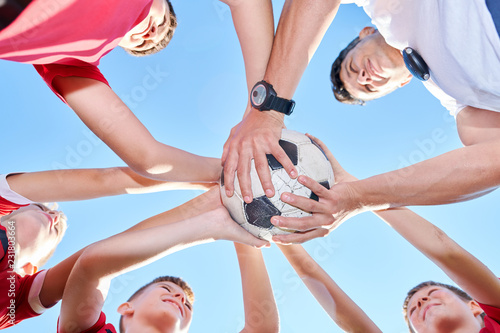 Low angle portrait of junior football team standing in circle and holding ball while huddling before match