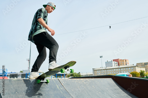 Full length portrait of contemporary young man doing longboard stunts on ramp in skateboarding park, copy space