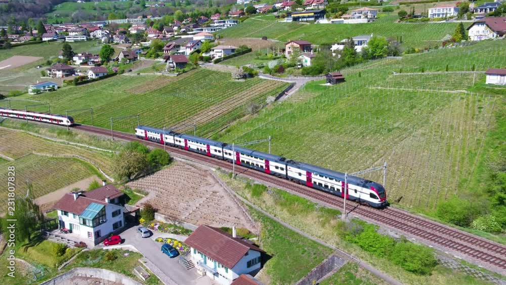 Aerial of two Swiss trains crossing in Lavaux vineyard, shot follows one passing over old viaduct. Lake L√©man and the Alps appearing in the background at the end