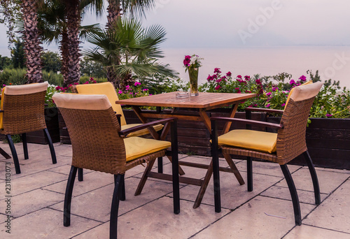 A cozy cafe on the terrace in the restaurant, overlooking the sea and tropical plants. Service for holidays and weekends. Vacation at the sea and dinner at the restaurant. © Katerina Tretiakova