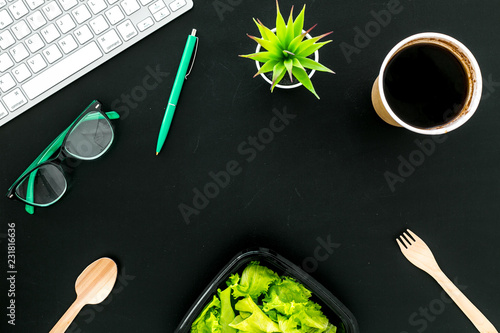 Order healthy food delivery to office. Light, diet meal with lettuce in plastic containers, coffee near computer keayboard and glasses on black background top view copy space photo