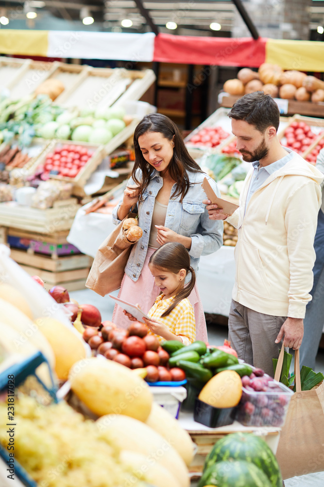 Positive young family standing at food shelves and using online