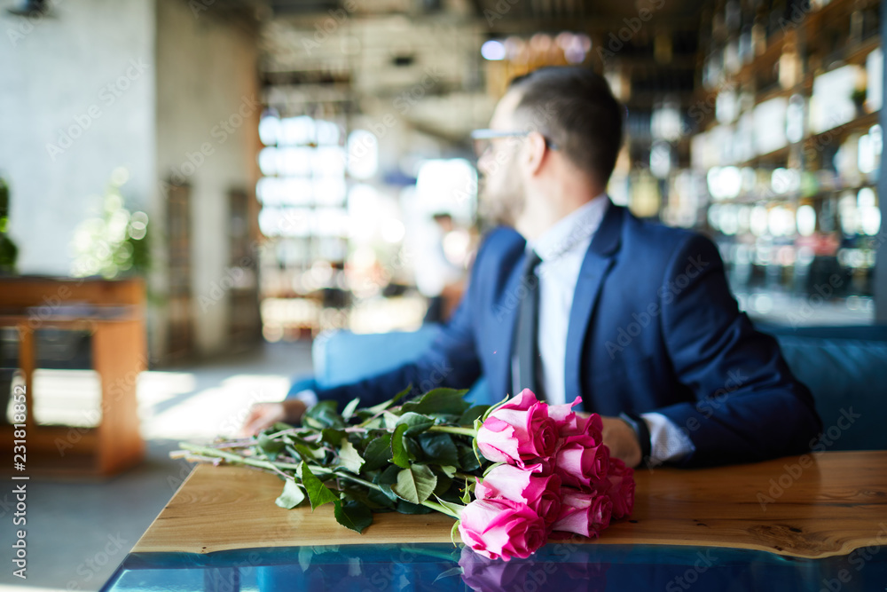 Fresh pink roses on table and elegant man sitting near by and waiting for his girlfriend Fresh pink roses on table and elegant man sitting near by and waiting for his girlfriend