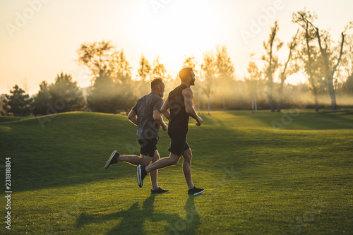 The two sportsmen running on the grass in the park on the sunny background