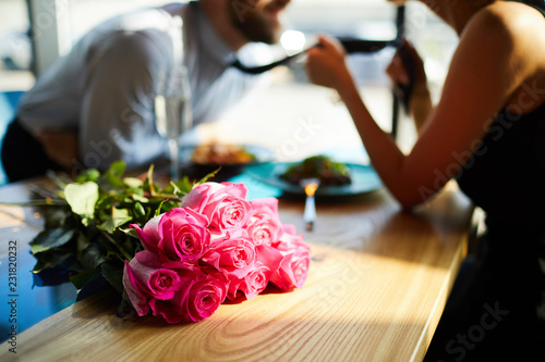 Fototapeta Fresh romantic roses on table on background of amorous man and woman flirting