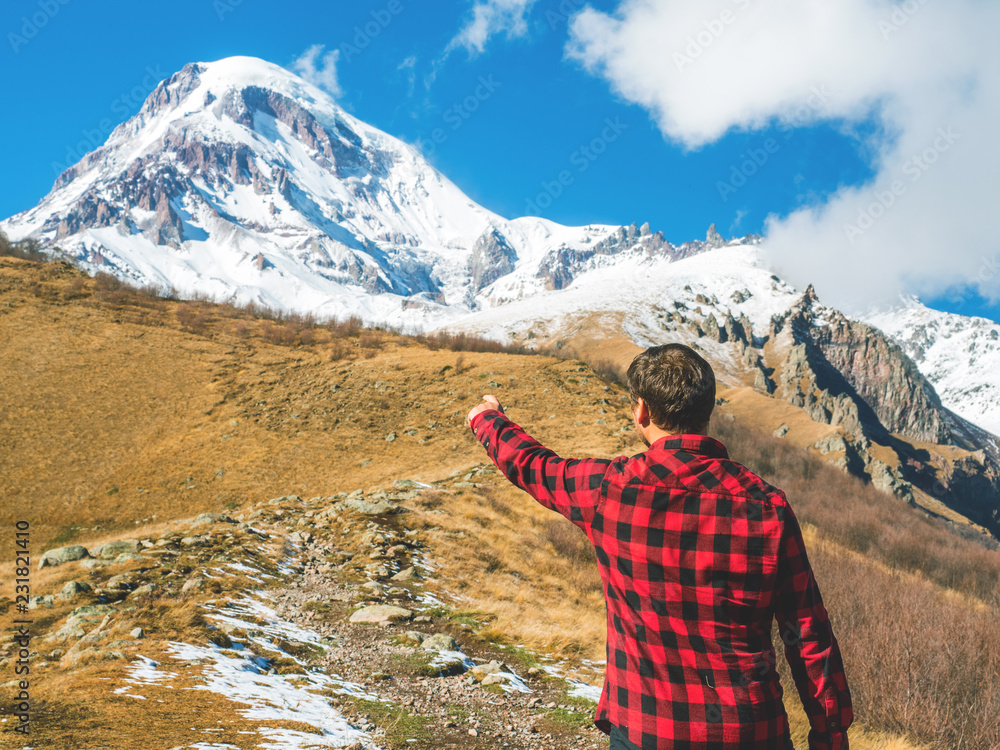 Traveler man points to the top of the mountain, standing back. Travel lifestyle, holiday vacation concept