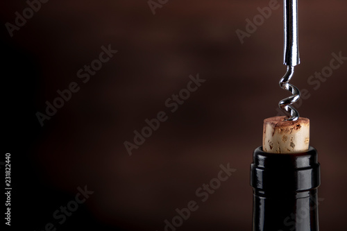 A closeup of a corkscrew pulling a cork from a bottle of wine on a dark background with a place for text