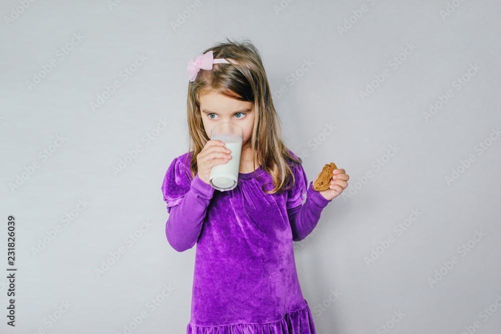 little girl drinking milk with cookies on a gray background of isolate. little girl drinking milk with cookies on a gray background of isolate.