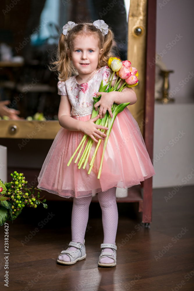 blue-eyed cute girl in a pink dress holding in her hands an armful of tulips