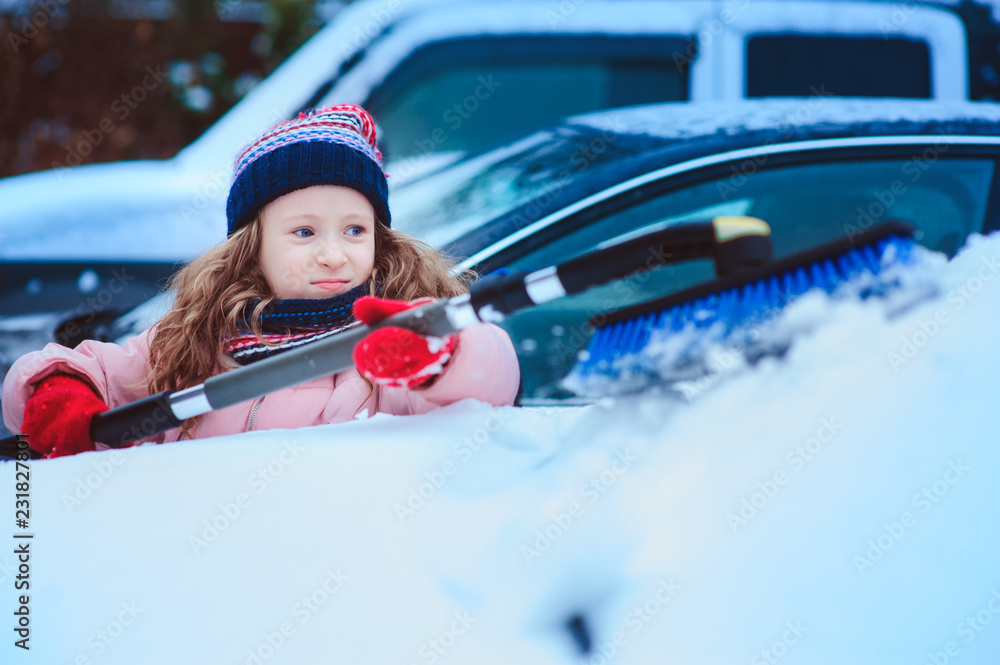kid girl helping to clean car from snow on winter backyard or parking. Car covered with snow after blizzard kid girl helping to clean car from snow on winter backyard or parking. Car covered with snow after blizzard