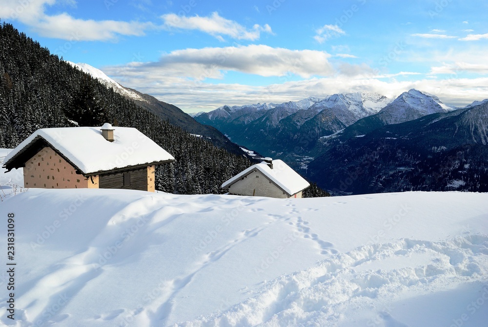Casette nella neve con panorama alle spalle con cielo azzurro e nuvole bianche