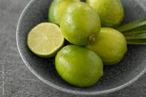 food  healthy eating and vegetarian concept - close up of limes in bowl on slate table top