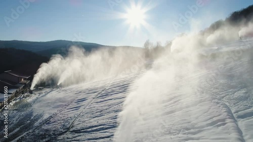 Aerial shot: The snow cannon's makes artificial snow on the slope of the mountain ski resort. Winter sports