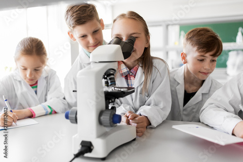 education  science and children concept - kids or students with microscope studying biology at school laboratory