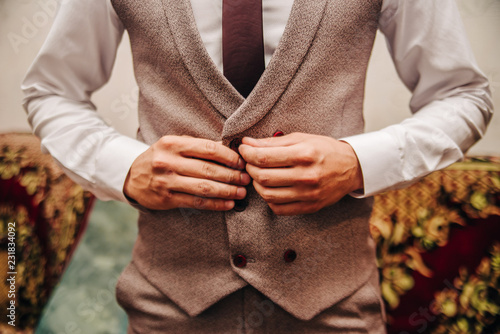 A man in a white shirt and gray vest buttons a button. Men's clothing. Stylish work suit. Business card.