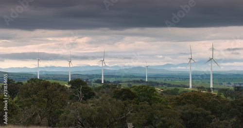 Wind turbines spinning in Australian bush-land against moody sky.