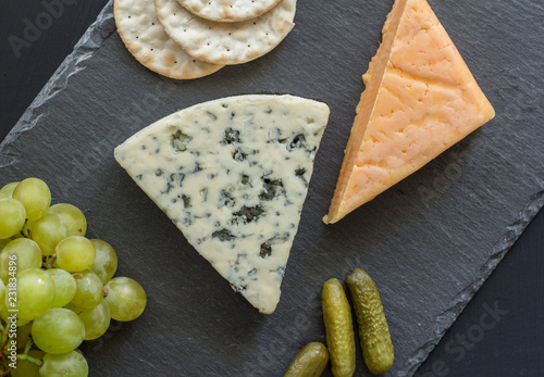 Fotografía Cheese board with blue cheese, cheddar cheese, green grapes, crackers and pickle