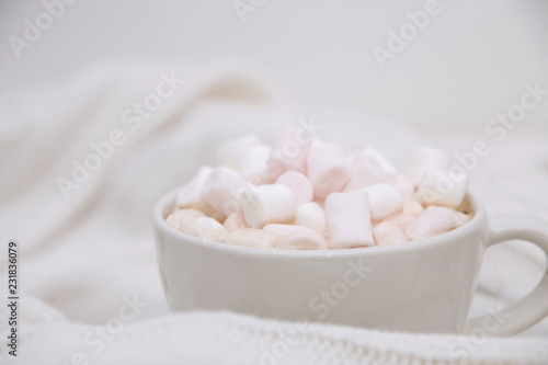 hot chocolate with marshmallows on a white knitted sweater. Copy space close up
