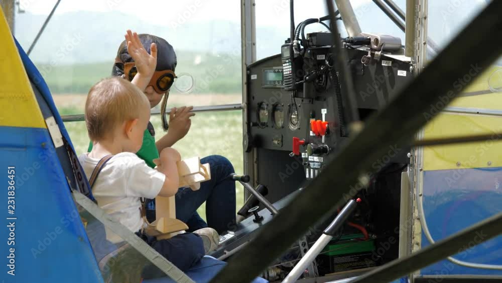 Brothers on board the plane, baby holding a toy, bigger child with pilot helmet Brothers on board the plane, baby holding a toy, bigger child with pilot helmet