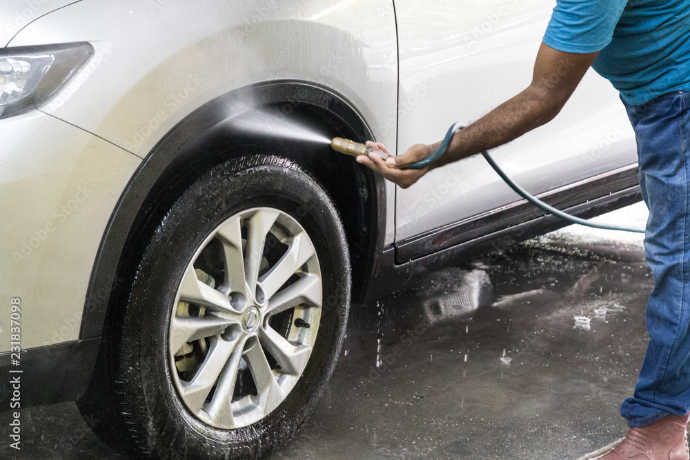 Worker spraying water onto car to wash