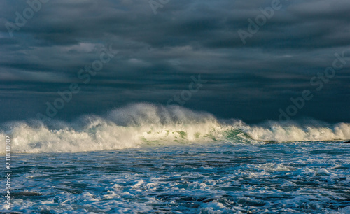 Powerful ocean wave on the surface of the ocean. Wave breaks on a shallow bank. Stormy weather  clouds sky background. Seascape.
