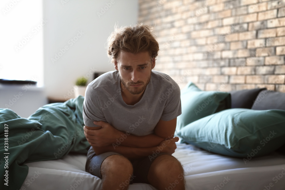 Depressed young man sitting on bed