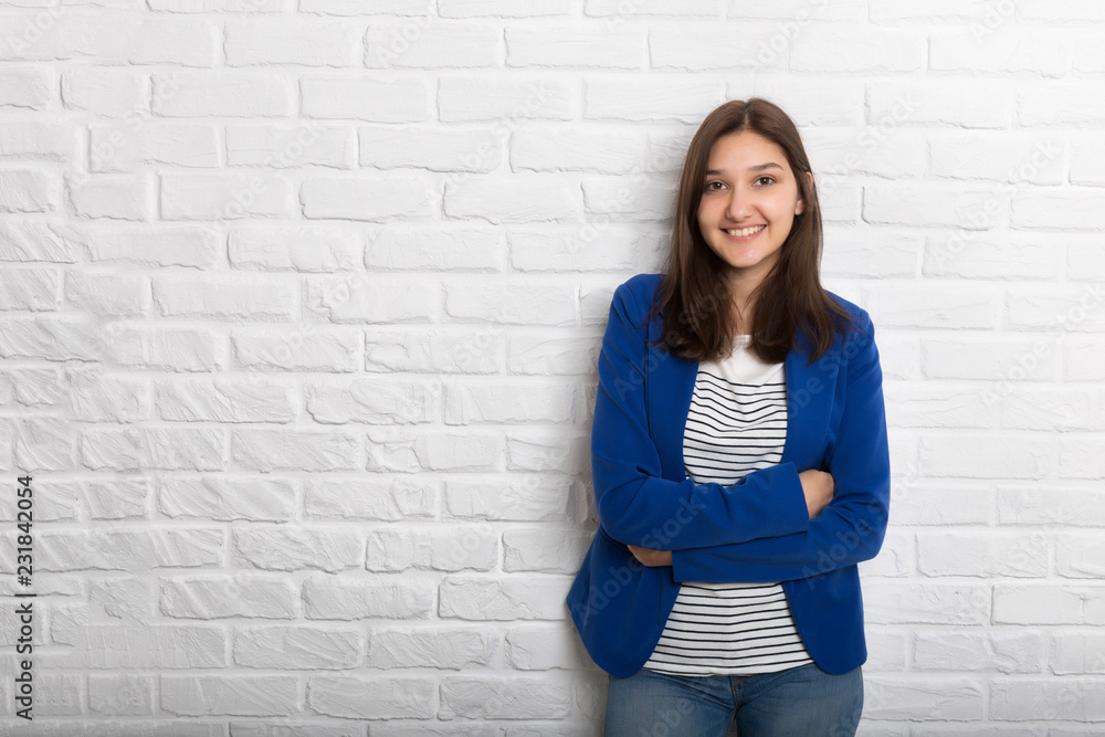 A young pretty smiling girl against a white loft-style brick wall. She looks at the viewer. Copy space. A young pretty smiling girl against a white loft-style brick wall. She looks at the viewer. Copy space.