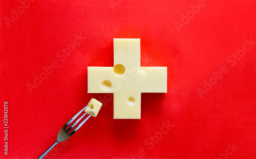 Swiss cross in form of cheese on red background, with a piece on fork photo