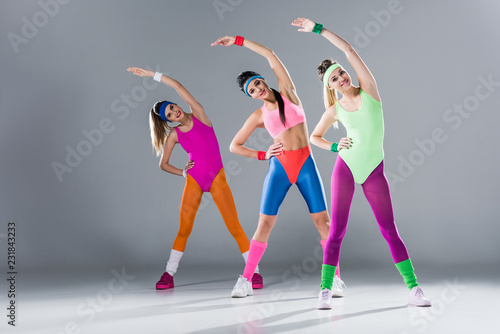 Fototapeta Naklejka Na Ścianę i Meble -  attractive sporty girls in bodysuits training at aerobics workout on grey