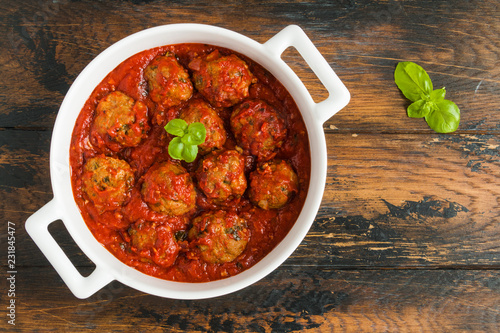 Meatballs cooked with tomato sauce in white casserole on wooden rustic table, top view photo