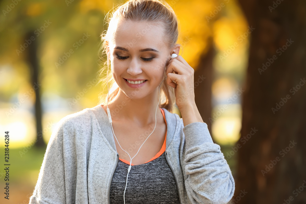 Sporty young woman listening to music in autumn park