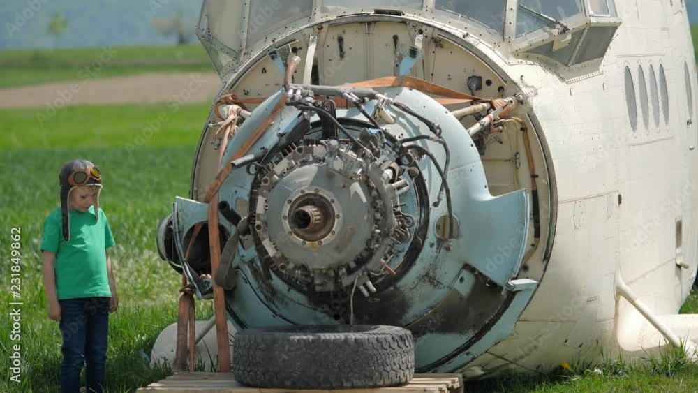 Funny child with pilot helmet looking at plane engine, difficult job Funny child with pilot helmet looking at plane engine, difficult job