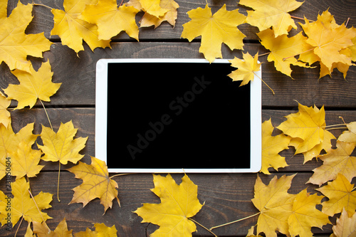 Mock up of tablet with black screen and yellow maple leaves on background. Autumn decor, fall mood.