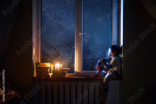  The child sits on the windowsill at night looking at the stars and dreams.