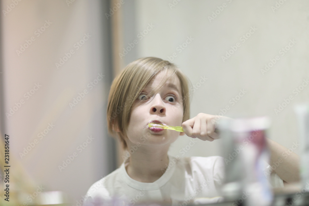 School-age boy with a stylish haircut brushes his teeth in front of a mirror in the dentist's office School-age boy with a stylish haircut brushes his teeth in front of a mirror in the dentist's office