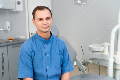 confident young dentist sitting in dentist office and looking at camera