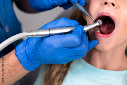 dentist with dental handpiece drilling teeth of little kid