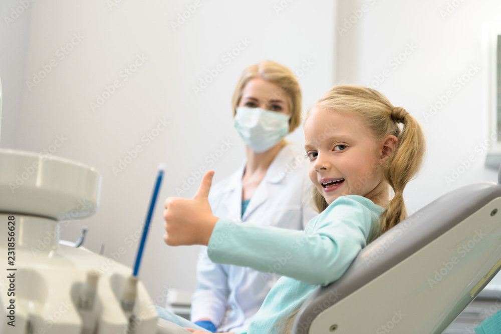 beautiful little child showing thumb up while sitting in chair at dentist office beautiful little child showing thumb up while sitting in chair at dentist office