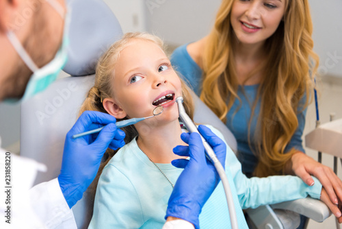 cropped shot of dentist working with little child while mother sitting near her for support