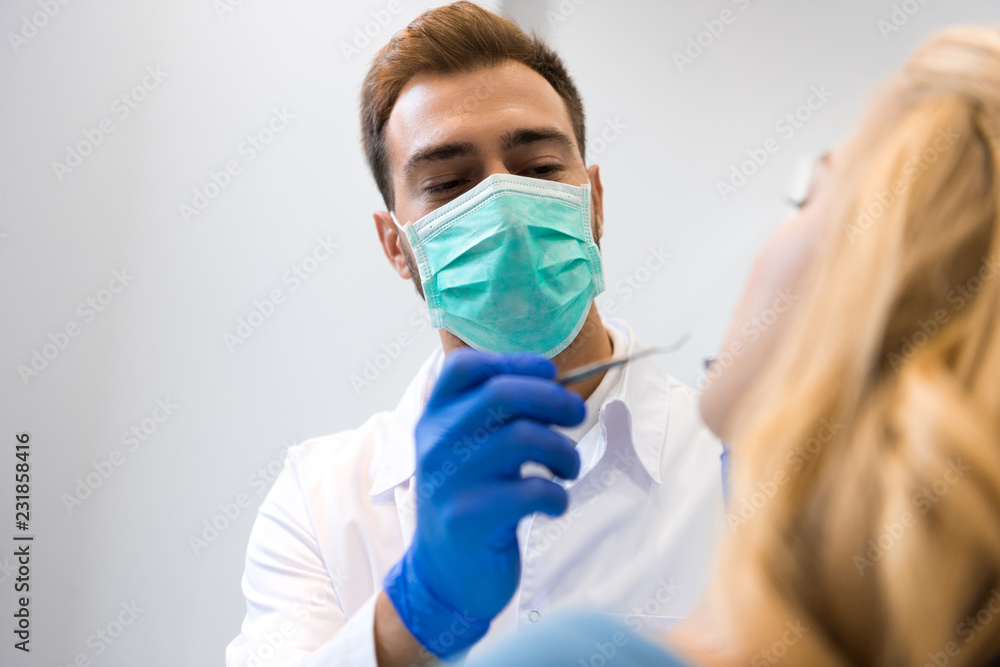 bottom view of young dentist in mask examining teeth of female client bottom view of young dentist in mask examining teeth of female client