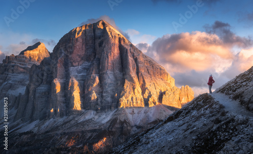 Young woman on the trail looking on high mountain peak at sunset in Dolomites  Italy. Autumn landscape with girl  path  rocks  sky with clouds at colorful sunset. Hiking in alps. Majestic mountains