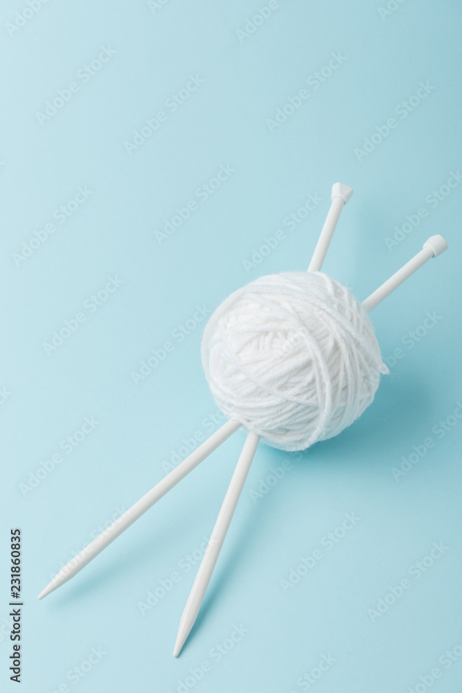 close up view of white yarn ball and knitting needles on blue background close up view of white yarn ball and knitting needles on blue background