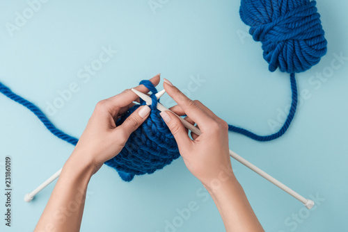 cropped shot of woman knitting on blue background with blue yarn photo