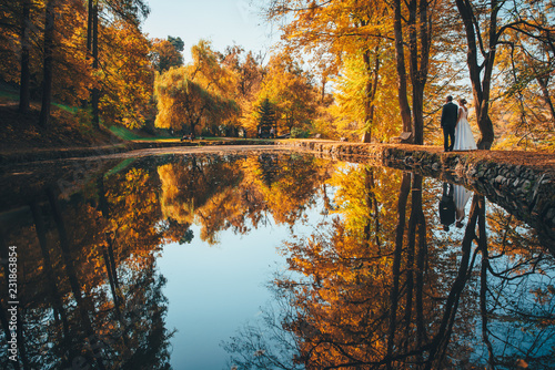 Fototapeta Naklejka Na Ścianę i Meble -  Bride and groom by lake in orange autumn park