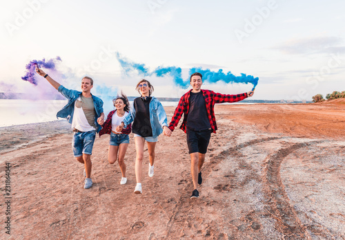 group of young friends running along the beach and holding hand flare or fusee. Freedom and independence concept