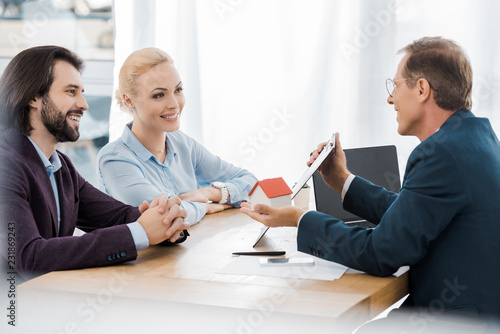 Wallpaper Mural adult smiling insurance agent showing contract and house model to young couple in office Torontodigital.ca