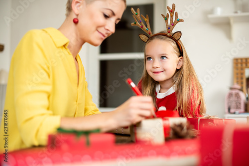 Mother and daughter having fun wrapping christmas gifts together in living room. Candid family christmas time lifestyle background. photo